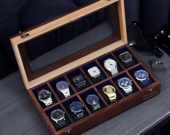 May include: A wooden watch box with a glass top, displaying a collection of wristwatches with various styles and colors. The box has a blue velvet interior and is made of dark wood with a light wood trim.