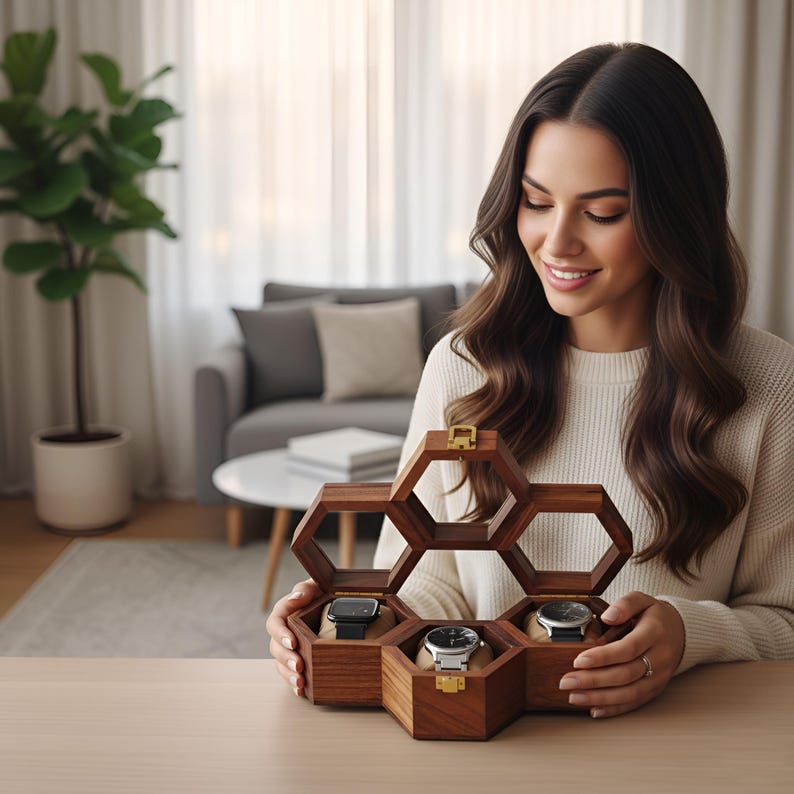 May include: A hexagonal wooden watch display case featuring three individual compartments, each containing a wristwatch on a beige cushion. The dark brown wooden box has gold-toned metal latches and hinges, with an open top section.