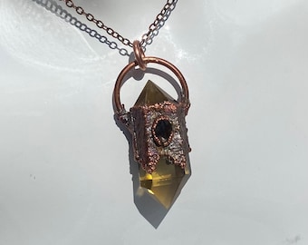 May include: A copper wire wrapped pendant with a clear, faceted, yellow crystal point and a black gemstone accent. The pendant hangs from a copper chain.