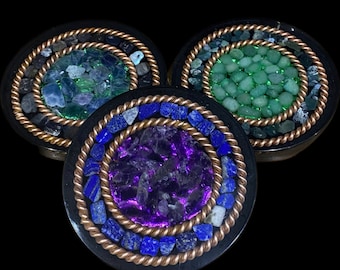 May include: Three round coasters with a mosaic design. Each coaster features a different color gemstone: green, purple, and blue.