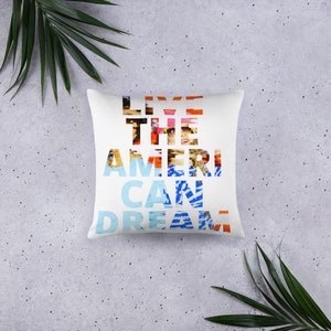 Puede incluir: Almohada blanca con el texto "Live the American Dream" en letras coloridas y superpuestas.