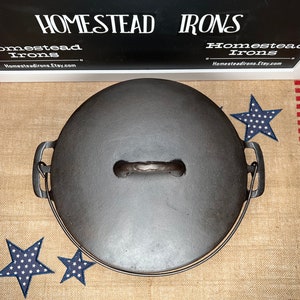 May include: A cast iron Dutch oven with a lid, featuring a handle and side handles. The oven is dark gray and sits on a burlap runner with red stripes and blue star accents. The sign at the top reads "HOMESTEAD IRONS".