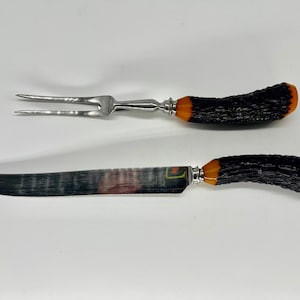 May include: A vintage carving set with black and orange handles. The set includes a knife and a fork.