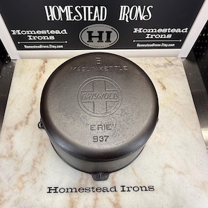 May include: A round, black cast iron Griswold Maslin Kettle, number 8, with the text ERIE and 937 embossed on the surface. The kettle features a central circular logo with the word GRISWOLD inside a cross design, showing a dark, textured finish.