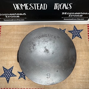 May include: A 9-inch cast iron skillet with the text "WAGNER" embossed on the bottom. The skillet is sitting on a burlap rug with red and white stripes and blue stars.