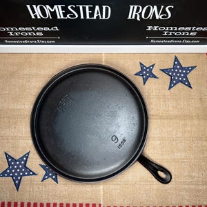 May include: A 9-inch cast iron skillet with a black finish and a handle. The skillet is sitting on a burlap fabric with red and white stripes. The skillet has the text "WAGNER" and "9 1508" on the bottom.