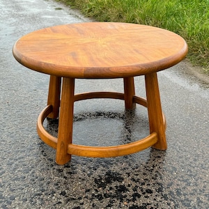 May include: A round wooden coffee table with a simple design. The table has a circular top and a base with four legs and a ring.