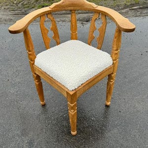 May include: A wooden corner chair with a white cushioned seat. The chair has a curved back and carved details on the legs and back.