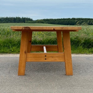 May include: A rustic wooden table with a natural finish. The table has a simple design with a rectangular top and four legs. The table is made of solid wood and has a natural grain pattern.