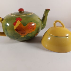 Peut inclure: Une théière verte avec un motif de coq et un sucrier jaune avec un couvercle. La théière a une poignée jaune et un bouton rouge sur le couvercle. Le sucrier a un couvercle jaune avec un bouton.