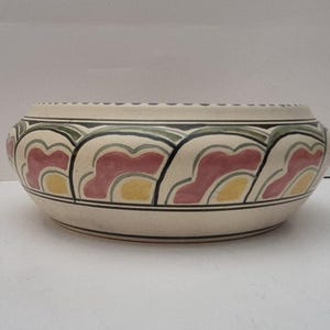 May include: A white ceramic bowl with a decorative design of pink, yellow, and green stylised flowers. The bowl has a rounded shape and a slightly flared rim.