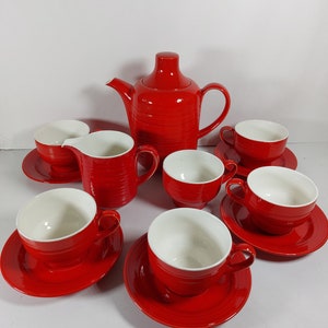 May include: A red and white tea set with a teapot, creamer, and six cups and saucers. The set has a ribbed design.