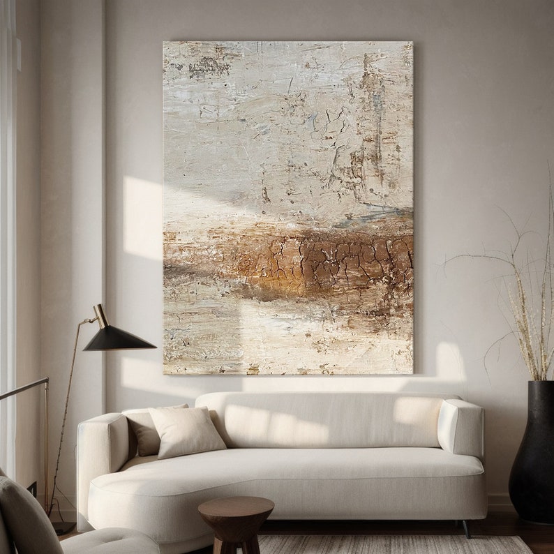 May include: Abstract painting with a brown and white color scheme. The painting has a textured surface and a horizontal band of brown across the middle. The painting is hanging on a wall in a living room setting.