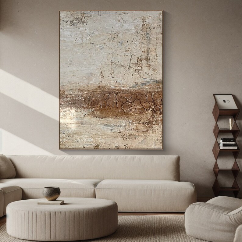 May include: Abstract painting with brown and white tones. The painting is framed and hanging on a wall in a living room setting.