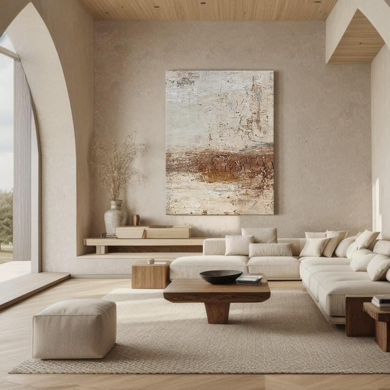 May include: A large abstract painting in beige and brown tones hangs above a modern sectional sofa in a minimalist living room. The sofa is white with beige cushions and is positioned in front of a wooden shelf.