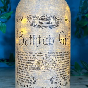 May include: A bottle of Ableforth's Bathtub Gin with a decorative label. The label features the text "Bathtub Gin" in large letters, along with detailed descriptions and illustrations of botanicals. The bottle is lit from within, creating a warm glow.