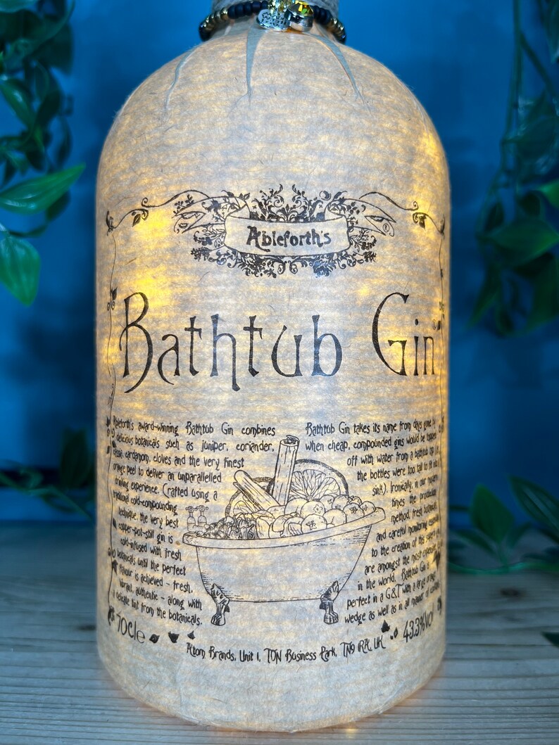 May include: A bottle of Ableforth's Bathtub Gin with a decorative label. The label features the text "Bathtub Gin" in large letters, along with detailed descriptions and illustrations of botanicals. The bottle is lit from within, creating a warm glow.