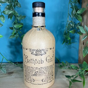 May include: A bottle of Ableforth's Bathtub Gin, wrapped in tan paper and twine. The bottle has a black wooden stopper and a decorative charm. The label features the text "Bathtub Gin" and a drawing of a bathtub.