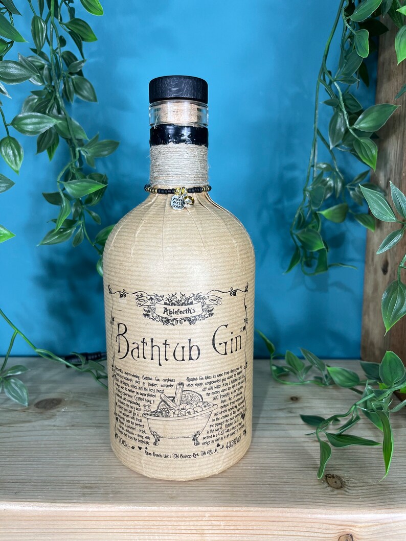 May include: A bottle of Ableforth's Bathtub Gin, wrapped in tan paper and twine. The bottle has a black wooden stopper and a decorative charm. The label features the text "Bathtub Gin" and a drawing of a bathtub.