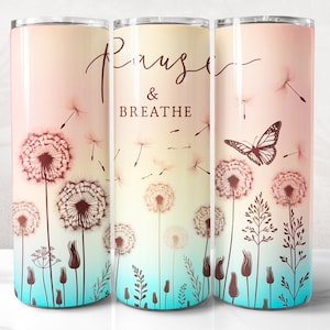 Può includere: Un bicchiere in acciaio inossidabile con uno sfondo sfumato rosa e blu. Il bicchiere presenta un design a dente di leone con una farfalla e il testo "Pause & Breathe".