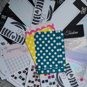May include: A collection of colorful polka dot paper bags, a black and white patterned card with the word "Dro" on it, and a pink and white patterned card with the word "Lebensmittel" on it. There are also several other cards and papers with various patterns and designs.