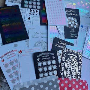 May include: A collection of black and white cards with silver and gold foil accents. The cards feature a Christmas tree design and the text "Der Baum Deiner Wunsche" (The Tree of Your Wishes). There are also cards with a budget sheet, a savings countdown, and a winter wonderland theme.