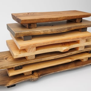 May include: A stack of five wooden serving trays with natural edges and a dark brown stain. The trays are stacked in a pyramid shape, with the largest tray at the bottom and the smallest tray at the top. Each tray has four small wooden legs.