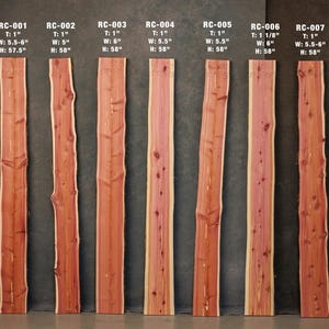 May include: Seven vertical red cedar wood planks with natural live edges, labeled RC-001 through RC-007. Each board displays unique wood grain, knots, and dimensions in inches, ranging from 5 to 6 inches wide and 57.5 to 58 inches in height.