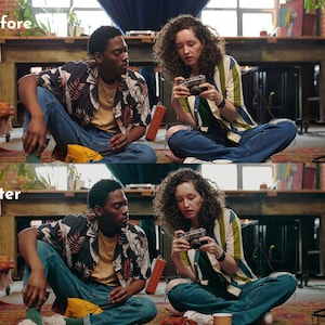 May include: Two people sitting on a rug, one holding a vintage camera. The person on the right is wearing a striped shirt with blue jeans. The person on the left is wearing a floral shirt and blue jeans. The scene is indoors with a table and other items in the background.