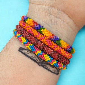 May include: A stack of colorful beaded bracelets in red, orange, yellow, blue, and purple. The bracelets are stacked on a person's wrist.