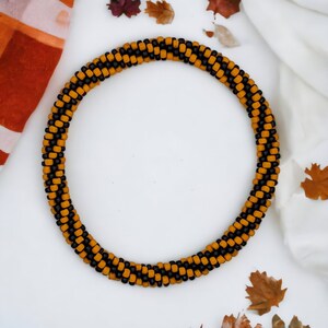 May include: A close-up of a necklace made of brown and gold beads. The necklace is lying on a white surface with autumn leaves scattered around it.