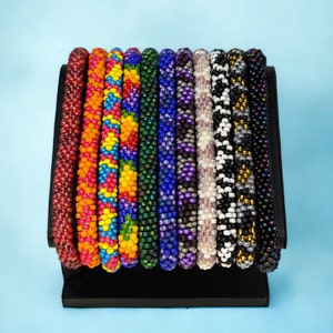 May include: A set of 10 colorful beaded bracelets, each with a unique pattern. The bracelets are displayed on a black stand against a light blue background.