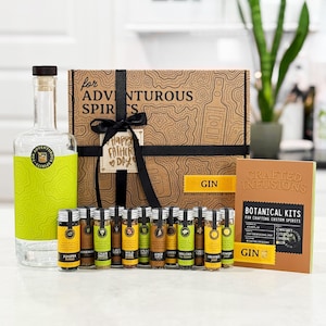 May include: A gift set for adventurous spirits, featuring a gin bottle with a green label, a box with a map design, and small glass vials of botanicals. The box is tied with a black ribbon and a "Happy Father's Day" tag.