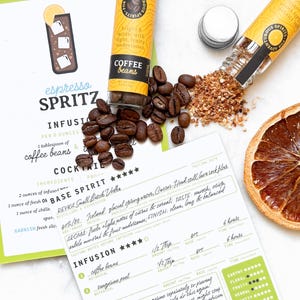 May include: An overhead shot features coffee beans, a recipe card for an espresso spritz cocktail, and a small jar of coffee beans. The recipe card includes ingredients and tasting notes. A dried orange slice adds color.