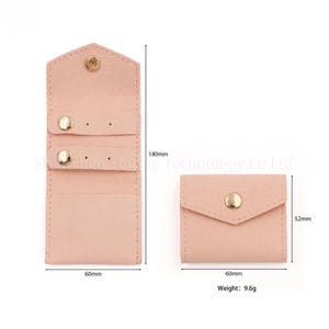 May include: A light pink, suede-like jewelry organizer with a snap closure. The open organizer is 140mm tall and 60mm wide, with two rows for earrings. A smaller, closed pouch is also shown, 52mm tall and 60mm wide. Weight: 9.6g.