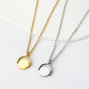 May include: Two necklaces with circular pendants. One is gold-toned, the other silver-toned. Each pendant is suspended from a delicate chain. The pendants have a rotating design, adding a unique element to the jewelry.