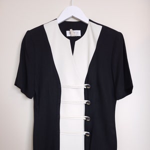 May include: A black and white dress with a V-neck and short sleeves. The dress has a white panel down the front with four gold buttons.