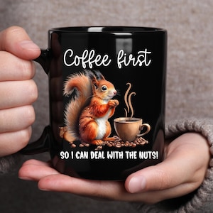May include: Black coffee mug with a white squirrel holding a cup of coffee and the text "Coffee first so I can deal with the nuts!"