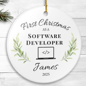 May include: A white, round Christmas ornament with the text "First Christmas as a Software Developer" and the name "James" with the year "2025". The ornament features a laptop graphic and green leaf accents.