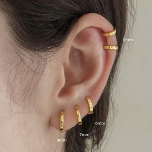 May include: Close-up of a person's ear adorned with multiple gold hoop earrings. The earrings vary in size, with measurements of 5mm, 6mm, 7mm, and 8mm. The image is from Amygrace Studio.