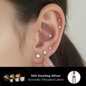 Op de afbeelding: Een oor met meerdere piercings, elk versierd met een kleine, sprankelende, heldere edelsteen. De afbeelding bevat de tekst "925 Sterling Silver Internally Threaded Labret".