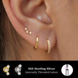Pode incluir: Um conjunto de três brincos dourados, incluindo um pino curvo com três pedras claras, uma argola lisa e uma argola com pavé. O produto é feito de prata esterlina 925 e apresenta um design de labret com rosca interna conforme ilustrado.