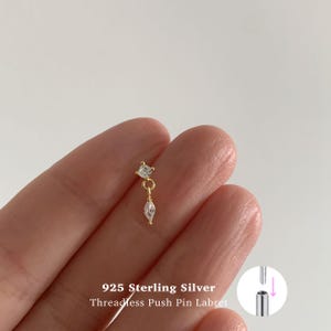 Könnte beinhalten: Ein goldfarbener 925 Sterling Silber Labret-Piercingstecker ohne Gewinde mit einem runden, klaren Stein und einem hängenden, marquise-geschliffenen klaren Stein. Der Text 925 Sterling Silver Threadless Push Pin Labret ist unten zu sehen.