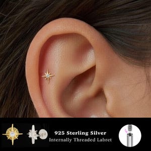 May include: A gold-toned starburst-shaped earring stud with a central clear stone, worn in the upper ear cartilage. The product is a 925 sterling silver internally threaded labret, shown from the front and side with a detailed screw mechanism.