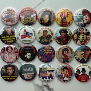 May include: A collection of 1986-themed buttons featuring pop culture references. The buttons display images of celebrities, movie scenes, and phrases like "Bon Jovi," "ALF," and "Ferris Bueller." The buttons are round and colorful.