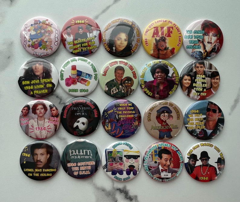 May include: A collection of 1986-themed buttons featuring pop culture references. The buttons display images of celebrities, movie scenes, and phrases like "Bon Jovi," "ALF," and "Ferris Bueller." The buttons are round and colorful.