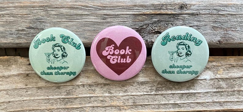 Pode incluir: Tr&ecirc;s bot&otilde;es redondos com um design vintage. Dois bot&otilde;es s&atilde;o verde claro com as palavras "Book Club" e "Reading" em uma fonte cursiva, uma ilustra&ccedil;&atilde;o retr&ocirc; e a frase "cheaper than therapy". O bot&atilde;o central &eacute; rosa com um cora&ccedil;&atilde;o bord&ocirc; e as palavras "Book Club".
