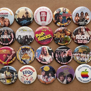 May include: A collection of vintage 1976 buttons featuring pop culture icons and logos. The buttons showcase bands like ABBA and Blondie, movies like Rocky, and TV shows like Charlie's Angels. Other buttons feature the Apple logo and the Bicentennial.
