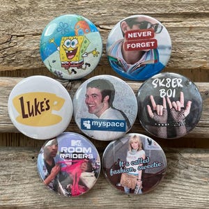 Op de afbeelding: Een verzameling van zeven ronde buttons met verschillende ontwerpen. E&eacute;n button toont SpongeBob SquarePants, een andere zegt "NEVER FORGET", en een derde heeft "SK8ER BOI" met handgebaren. Andere buttons zijn "Luke's" koffie, "myspace", "MTV Room Raiders" en "It's called fashion, sweetie."