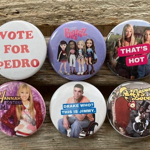 Op de afbeelding: Een verzameling van zes ronde buttons. De buttons tonen verschillende ontwerpen, waaronder teksten als "VOTE FOR PEDRO", "THAT'S HOT" en "DRAKE WHO? THIS IS JIMMY.", en afbeeldingen van Bratz-poppen, Hannah Montana en Flavor of Love.